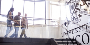 Three students walking down the staircase in the Joseph Banks Laboratories, with a large University of Lincoln crest on the wall to the right