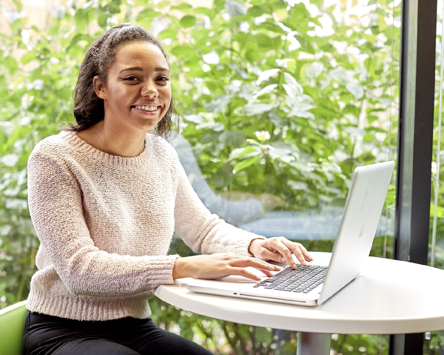 Student sat at a small round table, working at a laptop